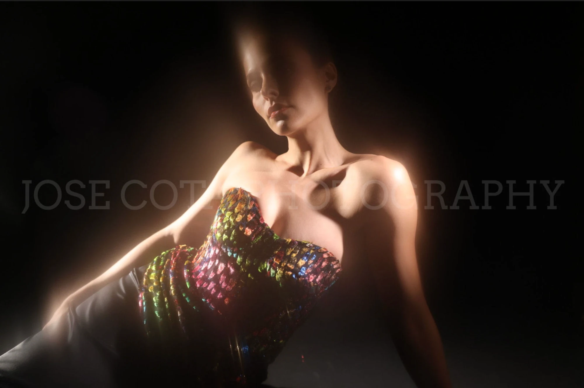 Modelo con corset iridiscente hecho a mano, iluminada en un estudio oscuro
